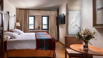 A hotel room with a bed, a TV, a table with a vase of flowers, and a view of the beach.