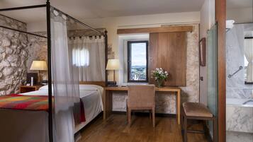 Une chambre à coucher avec un lit à baldaquin, un bureau avec une chaise, une vue par la fenêtre et une salle de bain avec un lavabo en marbre.