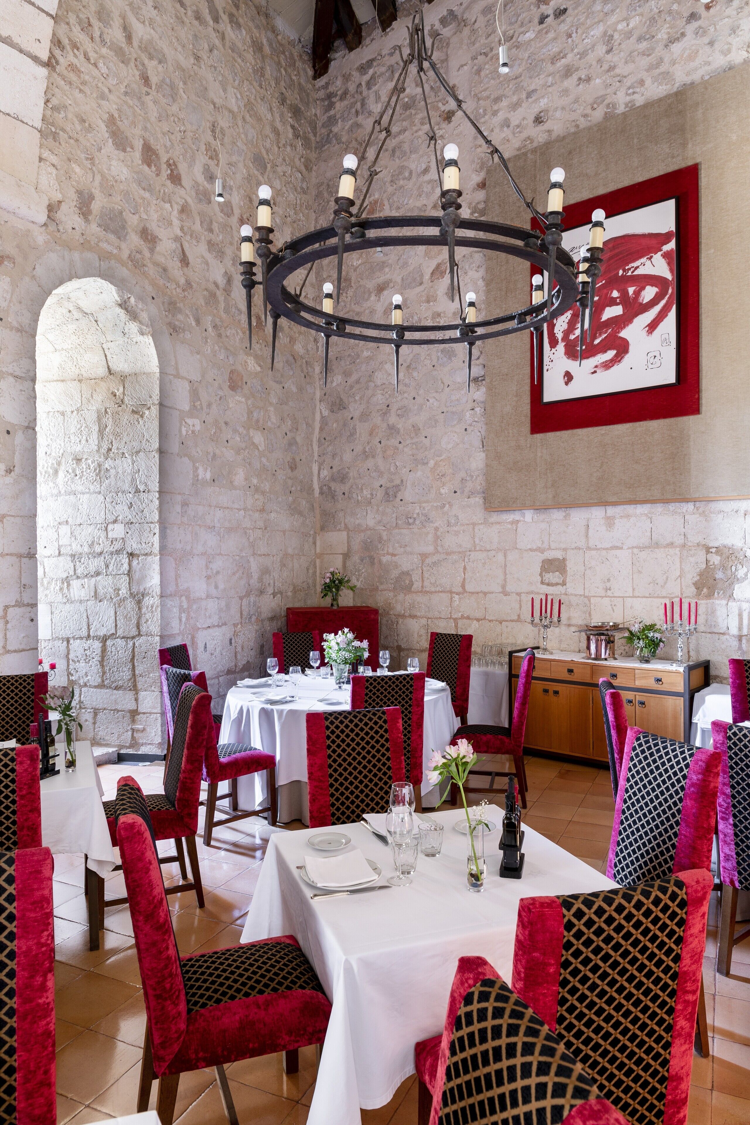 A restaurant with stone walls, a chandelier, and red and black upholstered chairs.