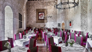 A restaurant with stone walls, white tables, and chairs with pink and black patterns. - Parador de Alarcón (Alarcon)