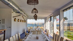 Una larga mesa de comedor dispuesta para una comida, con sillas a ambos lados, un centro de mesa decorativo y vistas al exterior a través de amplios ventanales.