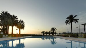 Una piscina tranquila con palmeras y una puesta de sol al fondo.