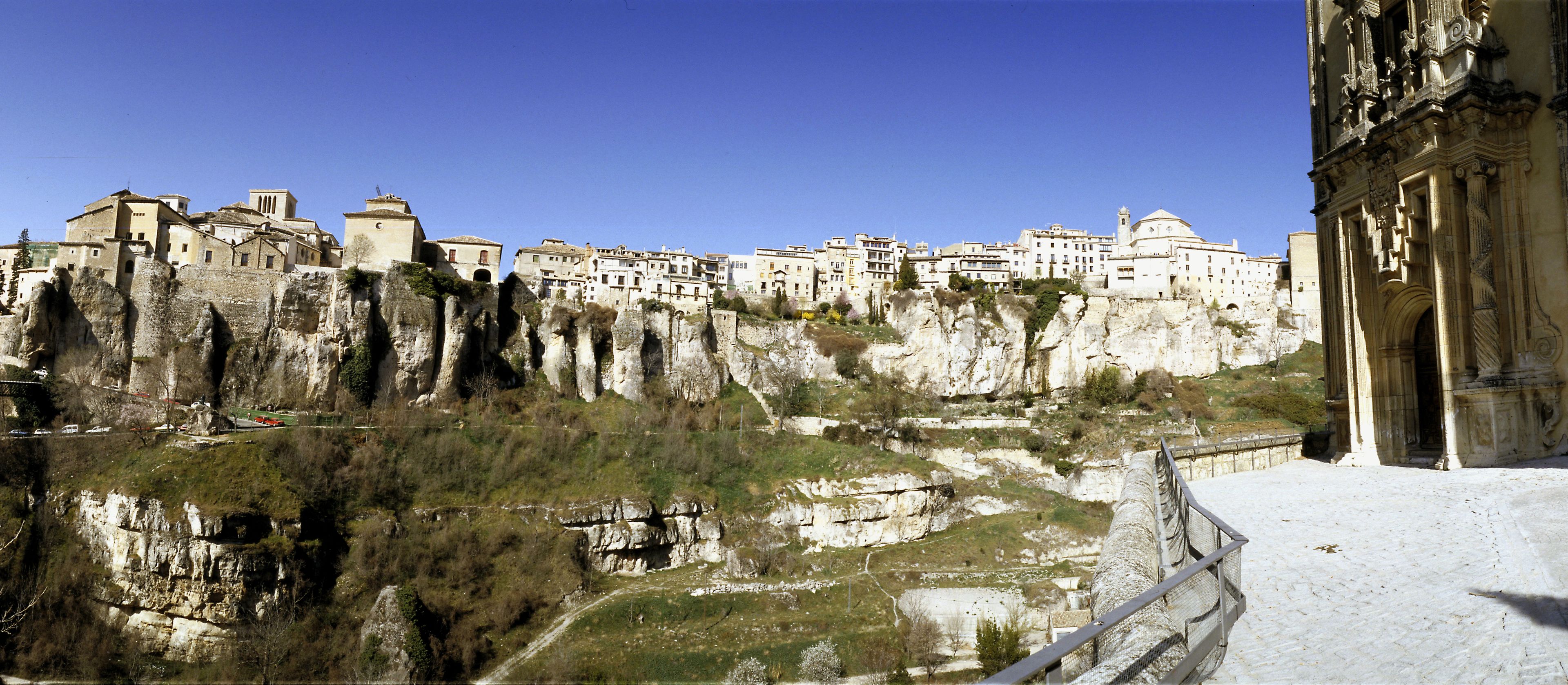 Un pueblo histórico con edificios encaramados a acantilados rocosos, cielo despejado y un camino que conduce a los edificios.