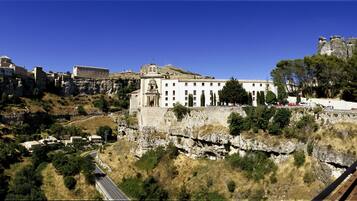 A historic building with a prominent central structure, surrounded by a hilly landscape and a railway track.