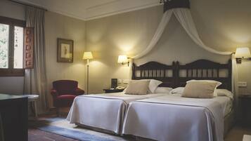 Une chambre d’hôtel avec deux lits, un fauteuil rouge, un bureau et une fenêtre avec des rideaux.