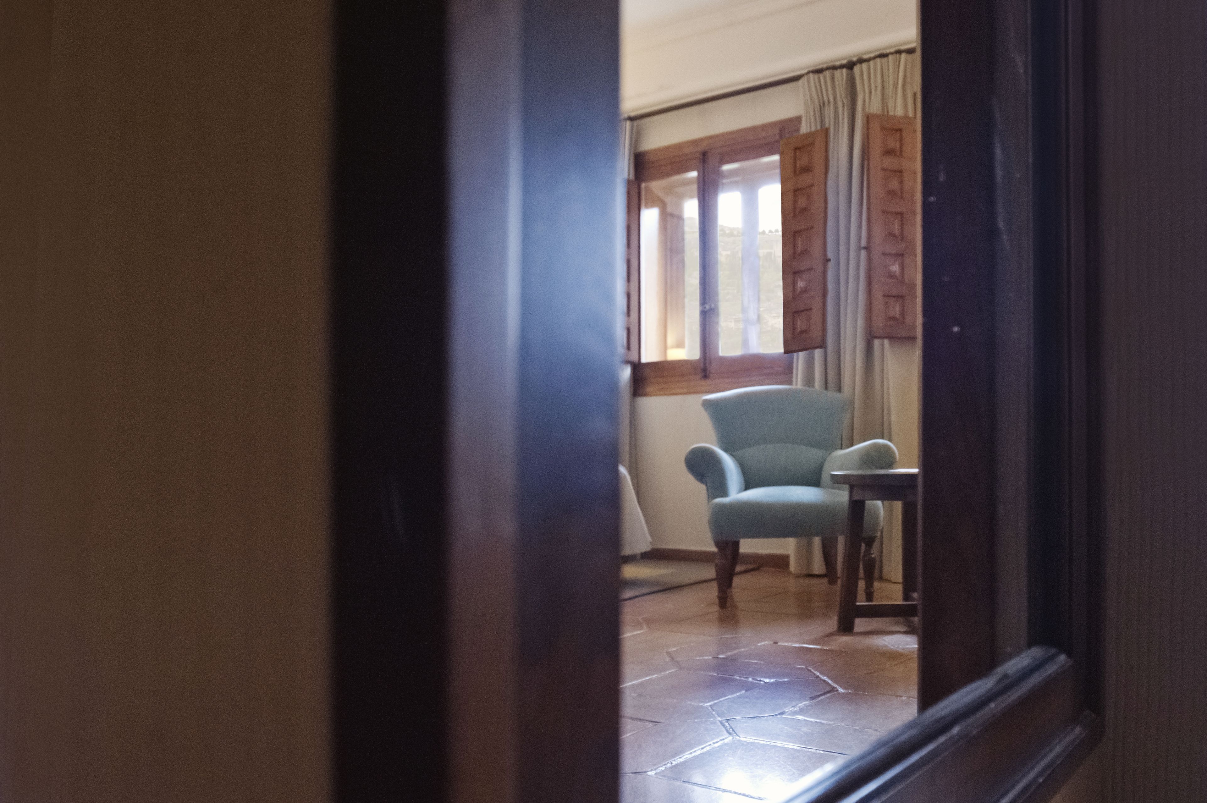 A room with a tiled floor, a chair, a table, and a window with curtains.