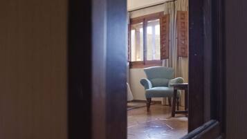 A room with a tiled floor, a chair, a table, and a window with curtains.