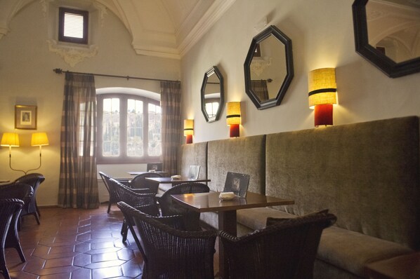 A dining area with wicker chairs, a wooden table, and a sofa. There are wall-mounted lamps and a large mirror.