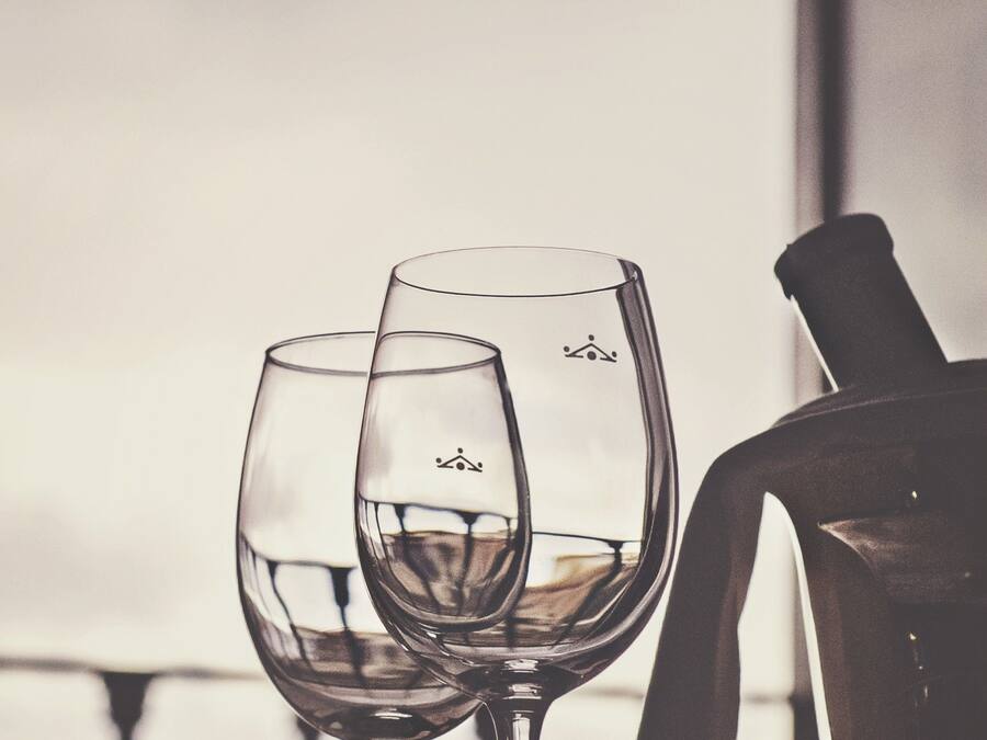 Two wine glasses on a table with a bottle of wine and a chair in the background.