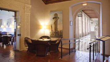 A lobby with hexagonal tiled flooring, wicker furniture, a painting of a lighthouse, and a staircase with a railing.