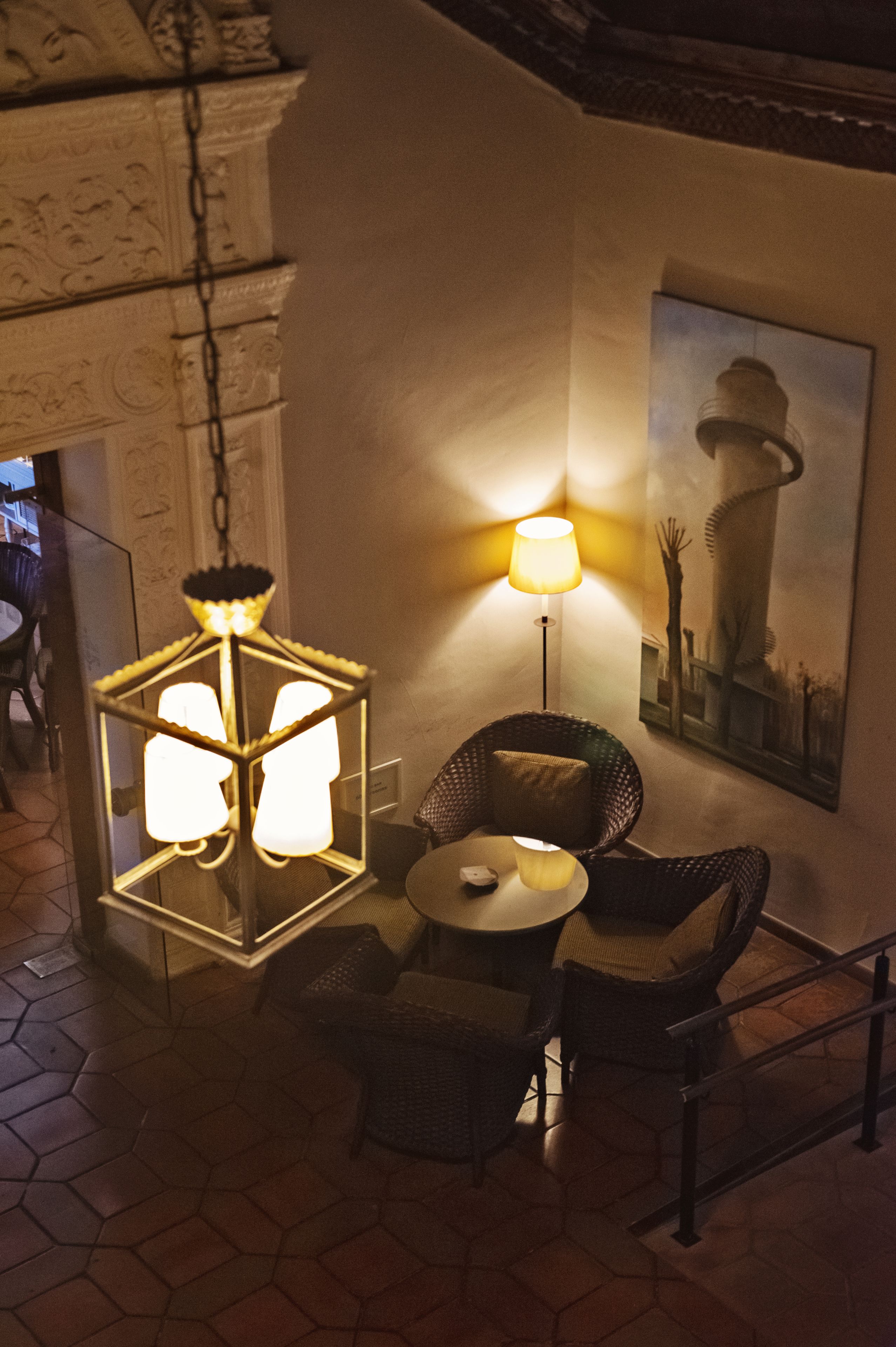 A cozy indoor seating area with hexagonal light fixtures, a round table, wicker chairs, and a wall-mounted lamp.