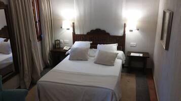 Habitación de hotel con una cama grande, dos mesitas de noche, un tocador, un espejo y una ventana con cortinas.
