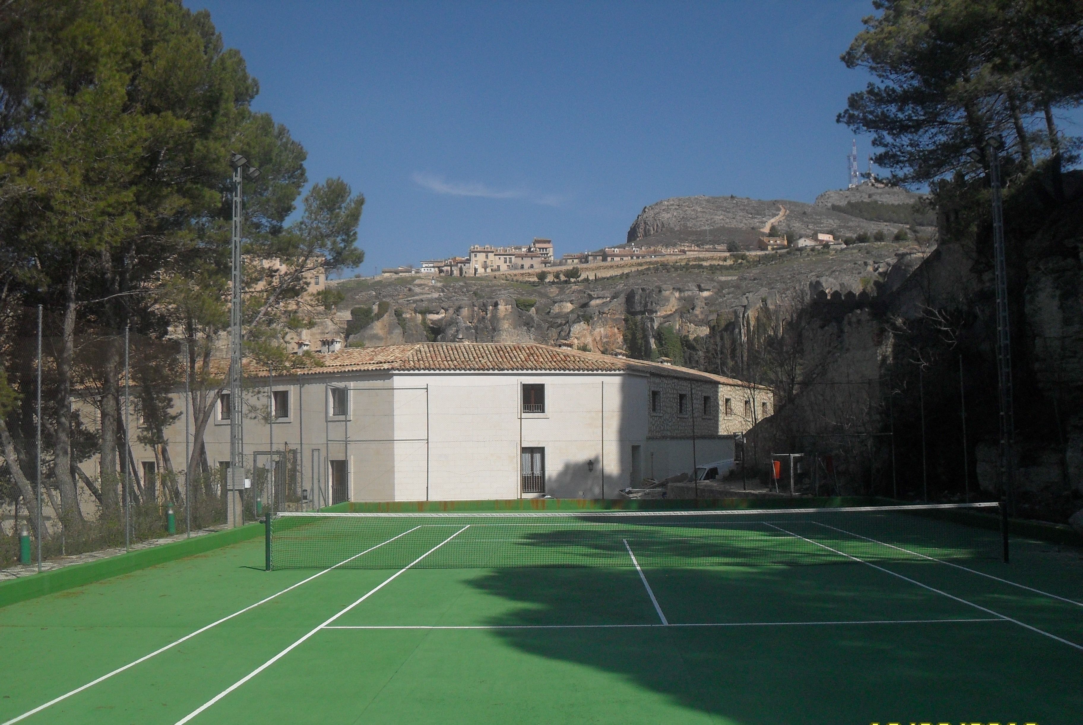 A tennis court with a net, surrounded by trees and buildings in the background.