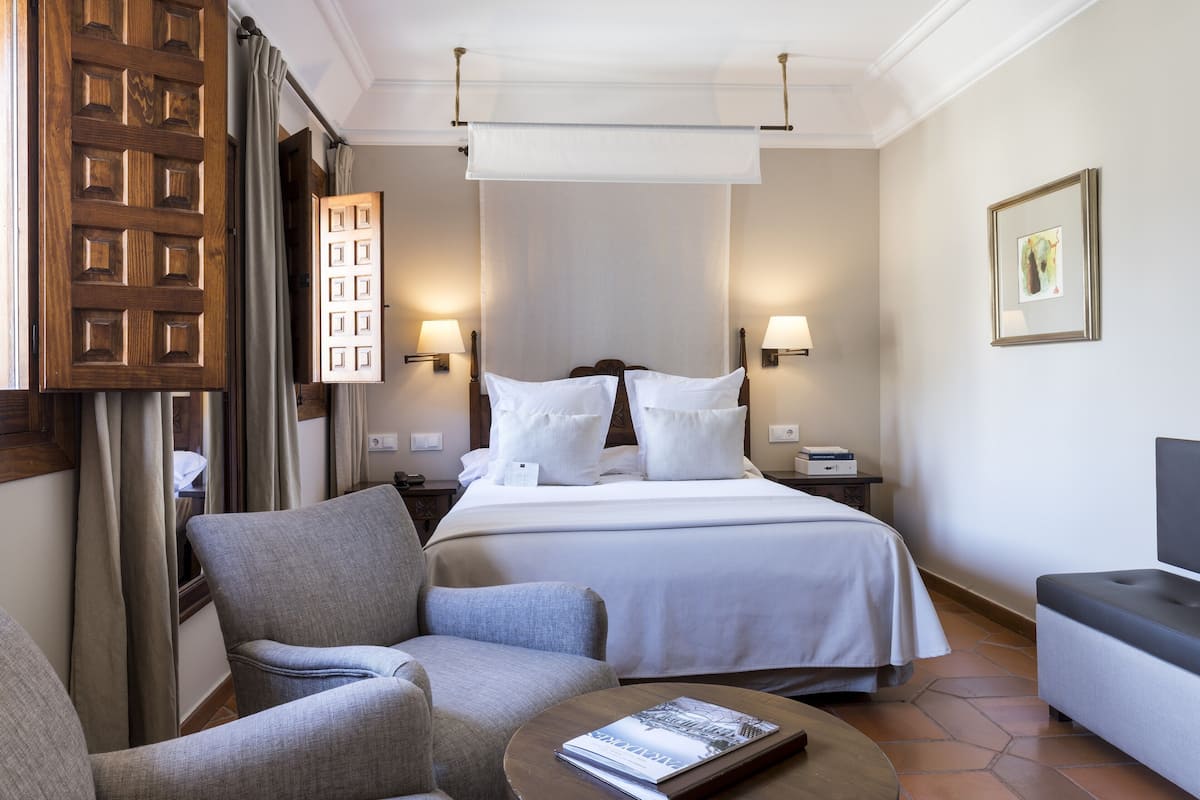 A hotel room with a large bed, two bedside tables, a chair, a sofa, and a small table with a magazine.