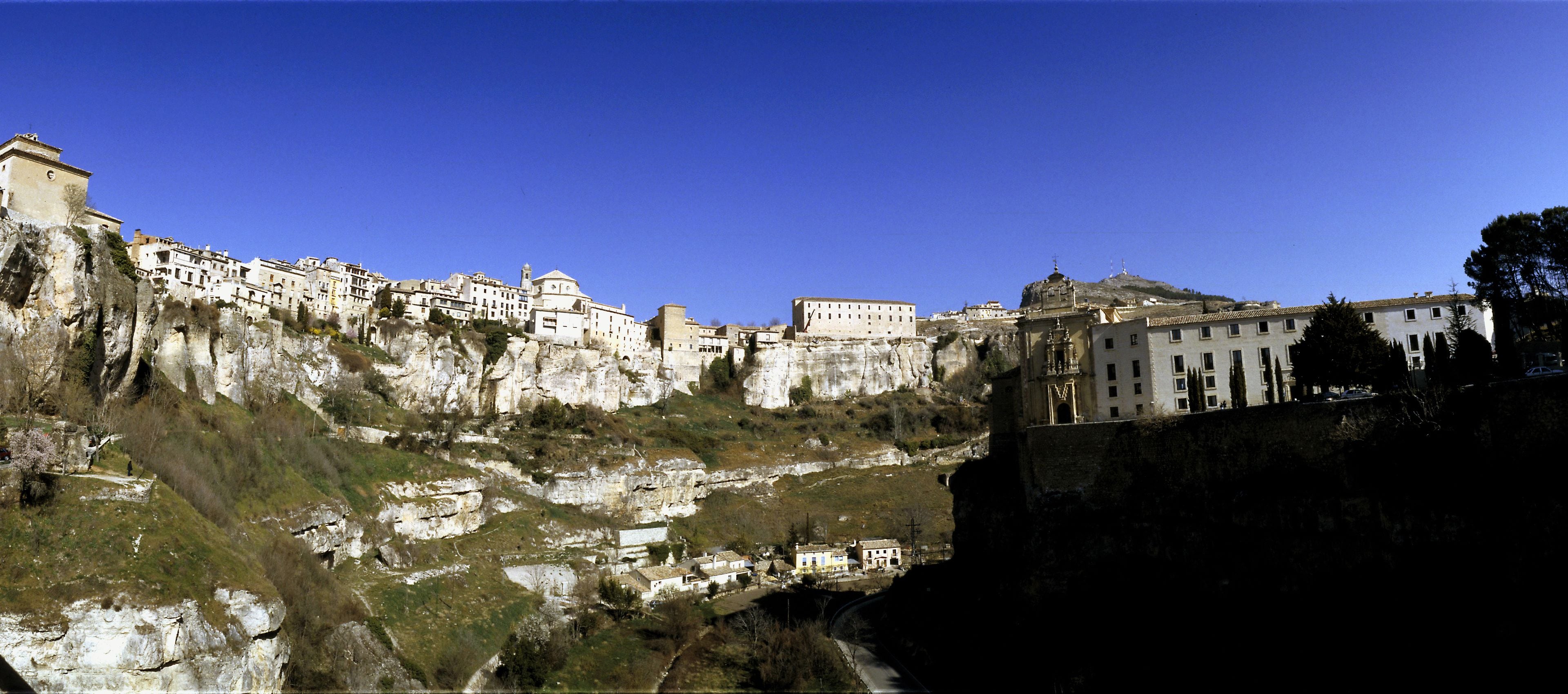 A historic town with buildings built into the hillside, featuring a prominent church and a large white building with a dome.