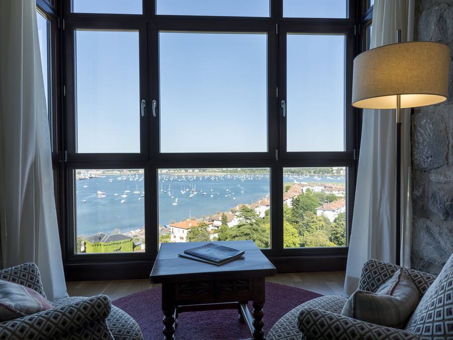 A room with a large window overlooking a marina, a table with a book, and patterned cushions.