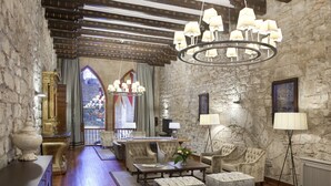 Une pièce spacieuse avec un mur en pierre, un plancher en bois et un lustre. On y trouve une table à manger avec des chaises, un canapé et un lampadaire.