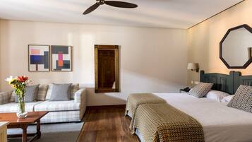 Habitación de hotel con cama, sofá, escritorio, espejo y obras de arte en las paredes.
