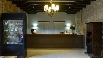 A reception area with a wooden counter, a chandelier, a glass display case with souvenirs, and a stone wall.