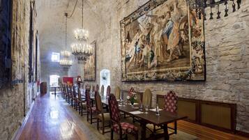 Una larga mesa de comedor con sillas, un candelabro y un gran mural en la pared.