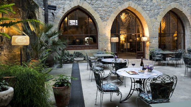 Une terrasse extérieure avec des murs en pierre, des fenêtres en arc de cercle et des meubles en métal.
