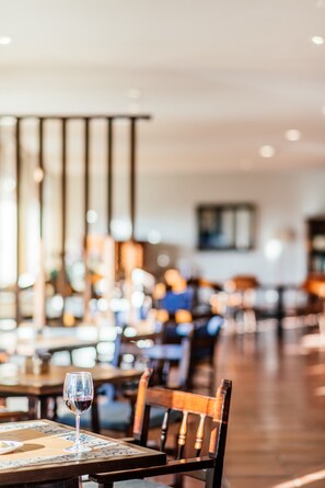 Interior de restaurante con mesas, sillas y una copa de vino tinto sobre una mesa.