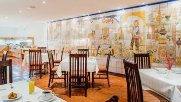 Un restaurante con mesas dispuestas para comer, sillas y una pared de azulejos con ilustraciones.