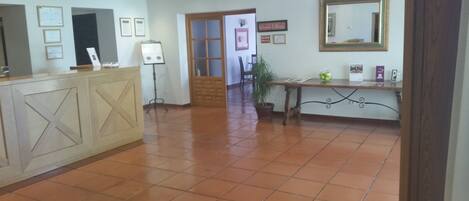 A reception area with a wooden reception desk, a potted plant, and a large mirror on the wall.