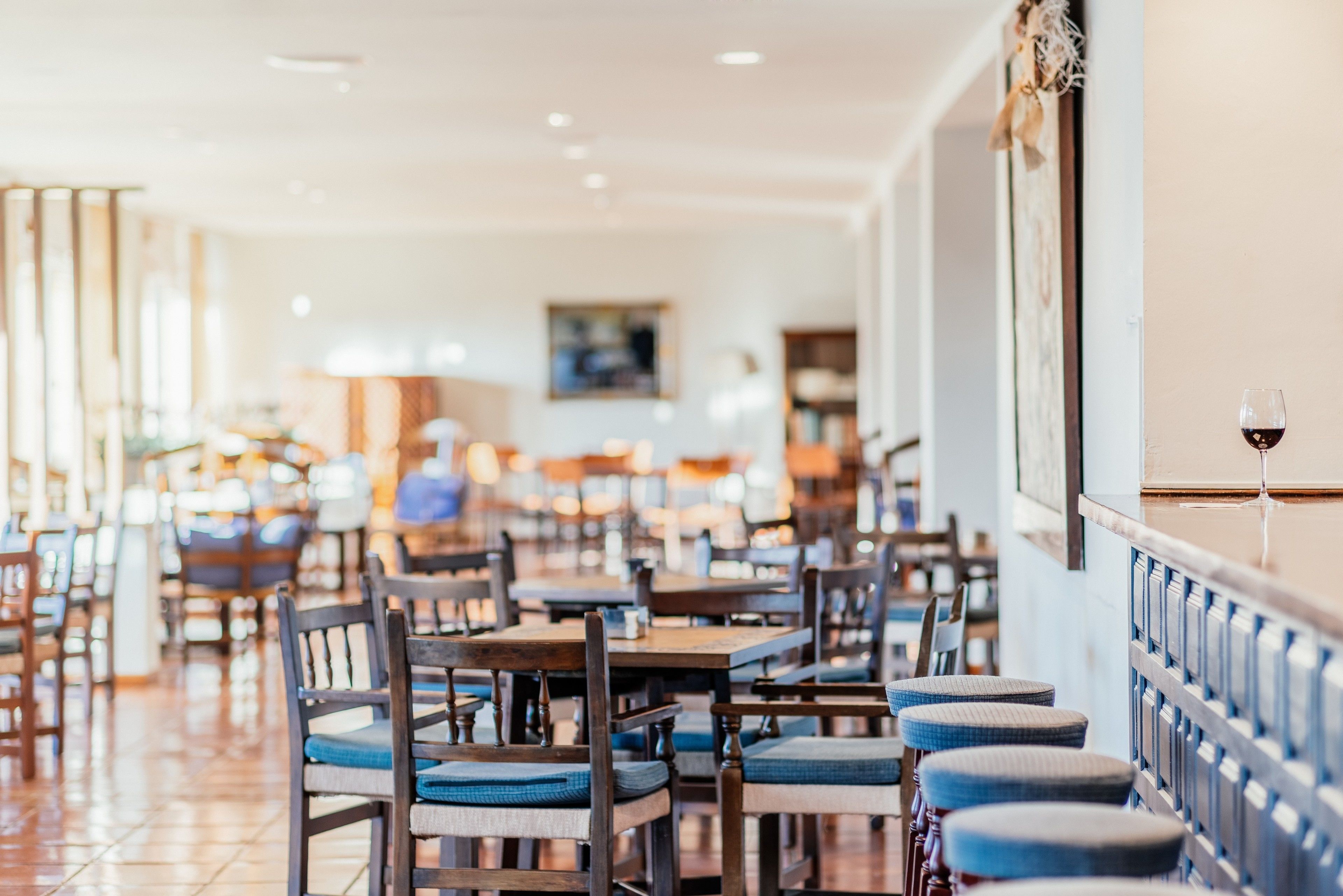 Un restaurante con mesas y sillas de madera, una copa de vino sobre una barra y un cuadro en la pared.