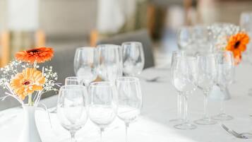 A dining area with tables set for a meal, featuring clear glassware and a vase with orange flowers.