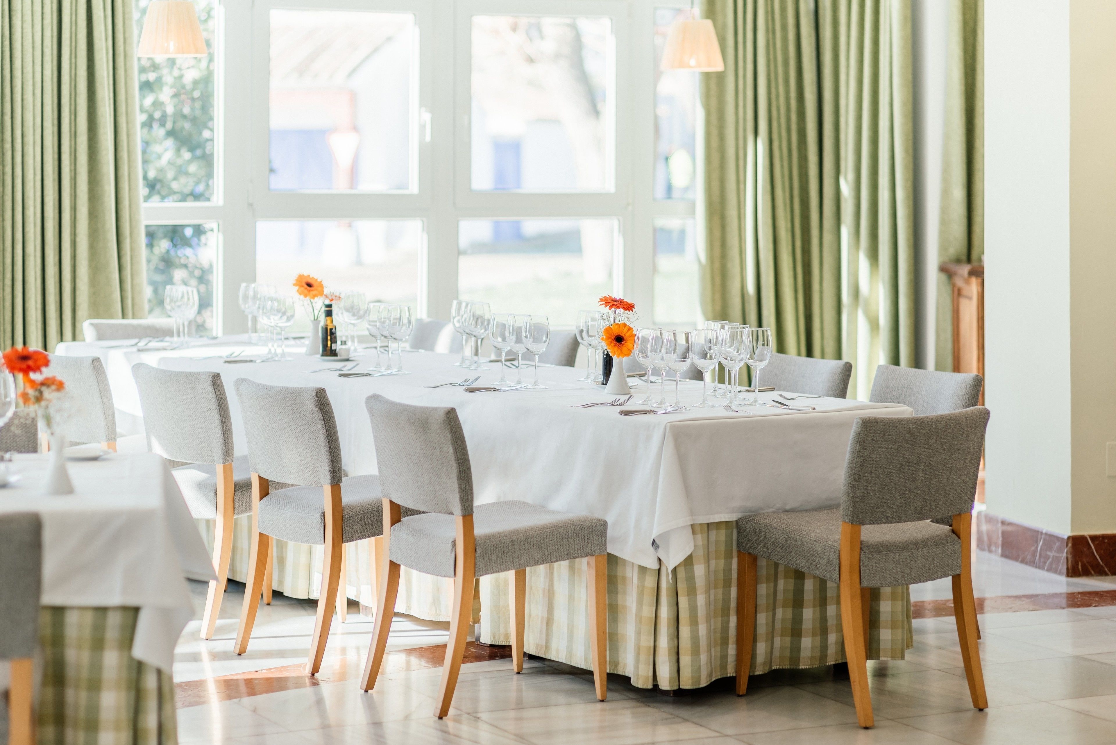 A dining area with round tables, grey upholstered chairs, and a white tablecloth.