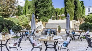 An outdoor patio with tables and chairs, surrounded by neatly trimmed hedges and trees. - Parador de Mérida (Merida)