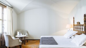 A hotel room with a bed, a chair, a small table, and a lamp.