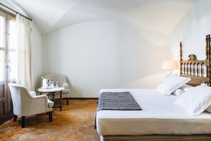 A hotel room with a bed, a chair, a small table, and a lamp.