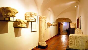 Un pasillo de museo con artefactos de piedra expuestos, techos abovedados y suelo de baldosas.