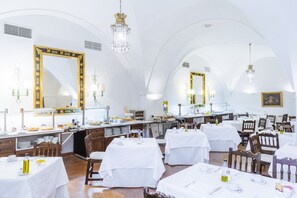 A spacious dining area with white tables and chairs, large mirrors, and chandeliers.