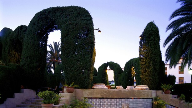 A landscaped garden with a fountain, steps, and various potted plants. - Parador de Mérida (Merida)