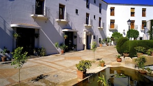 A courtyard with a pool, potted plants, and a white building with balconies. - Parador de Mérida (Merida)