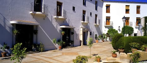 A courtyard with a pool, potted plants, and a white building with balconies.