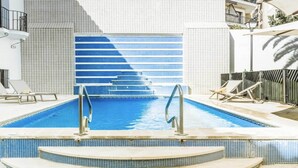 A swimming pool with steps leading into it, surrounded by lounge chairs and a lifebuoy.