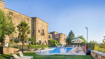 Zona de piscina con sillas de descanso, un edificio de piedra y cielo despejado.