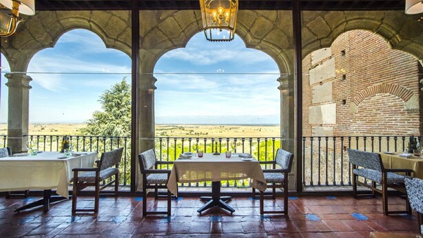 Une terrasse avec une table et des chaises, un mur en pierre en arc de cercle et une vue sur la campagne.