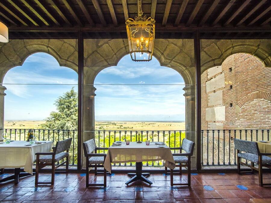 Een terras met een tafel en stoelen, een gewelfde stenen muur en uitzicht op het landschap.