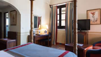 Habitación de hotel con cama con dosel, un escritorio con lámpara, televisor y una silla.