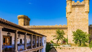 Un château historique en pierre, doté d’une tour ronde et d’une haute tour centrale, entouré d’une cour avec une galerie couverte et des colonnes.