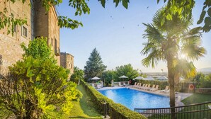 Une piscine avec des chaises longues, un palmier et un bâtiment à la façade en pierre.