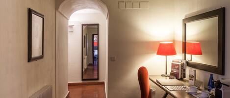 A hotel room with a desk, two red lamps, a mirror, and a chair.