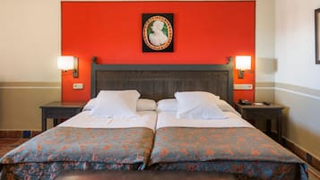 A double bed with a floral bedspread, two bedside tables, a nightstand, and a wall-mounted picture.