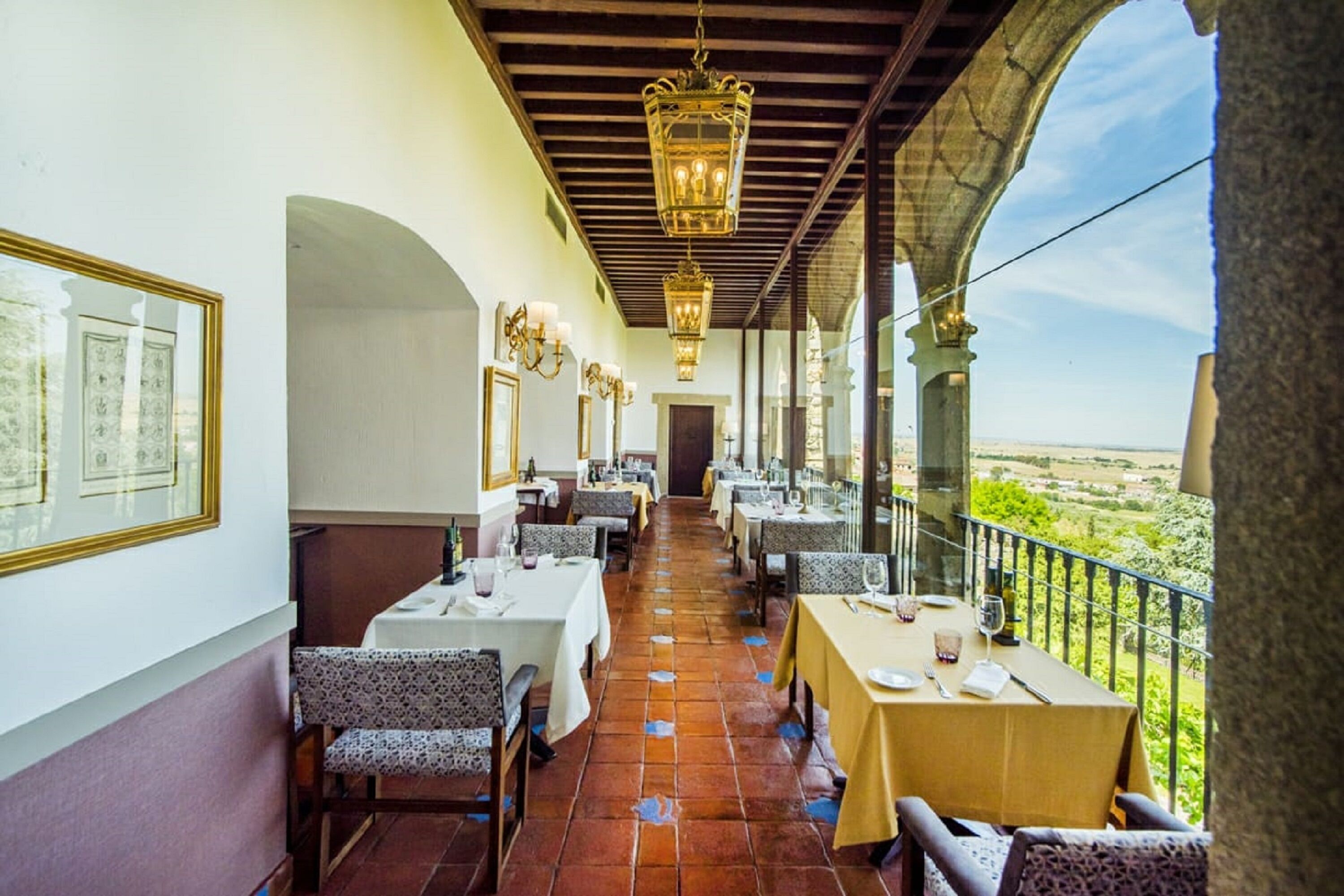 A restaurant with tables set for dining, a balcony with a view, and hanging lanterns.