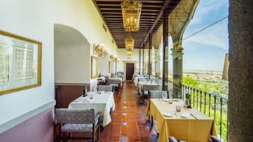 A restaurant with tables set for dining, a balcony with a view, and hanging lanterns.